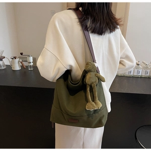 Detail of dark green canvas hobo bag with leather strap and plush frog charm on model