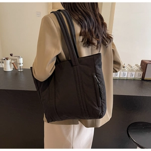 Detail of minimalist black fabric tote bag with side zipper pocket shown on model shoulder