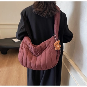 Deep burgundy quilted crescent shoulder bag with plush bear charm worn by model