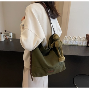 Detail of dark green canvas hobo bag with brown leather strap and a frog plush charm