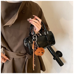 Detail of a black shiny PU leather barrel bag with silver hardware and a plush bear charm