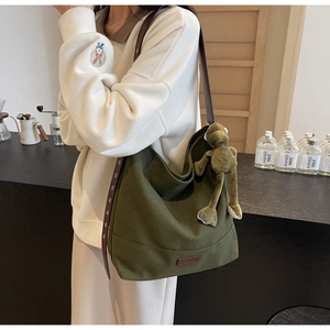 Detail of green canvas tote with brown leather base and cute plush frog charm accessory