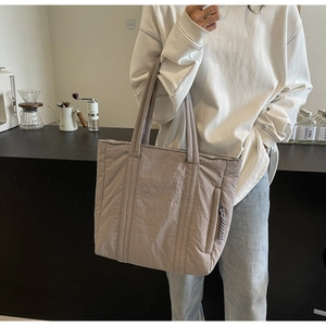 Detail of the pleated nylon tote bag texture and side zipper pocket on a beige shoulder bag