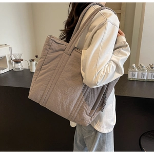 Detail view of large quilted grey fabric tote bag featuring textured nylon and woven zipper pull