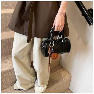 Detail of glossy black PU leather Boston bag featuring a cute brown plush teddy bear charm