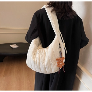 Detail view of quilted white crescent bag with plush bear charm on a female model
