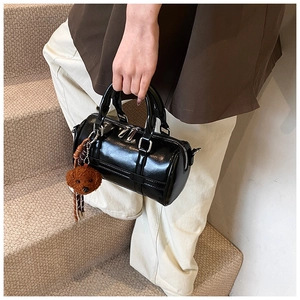 Detail of black patent leather boston bag with silver hardware and teddy bear charm