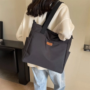 Minimalist black nylon tote bag for women with wide shoulder straps and orange logo tag