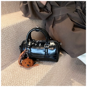 Close-up of shiny black PU leather boston bag with a cute brown teddy bear keychain