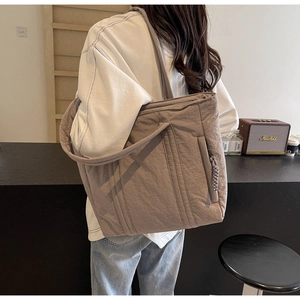 Detail of coffee nylon tote bag showing wrinkled fabric texture and shoulder strap on model