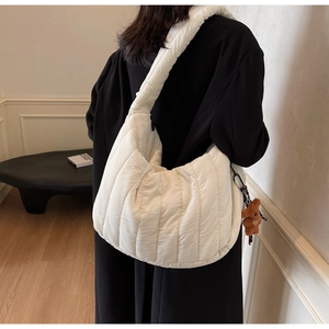 Detail of white quilted crescent bag with a cute brown plush bear charm and wide strap