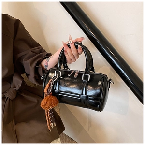 Detail of glossy black patent leather barrel bag with silver hardware and fur charm