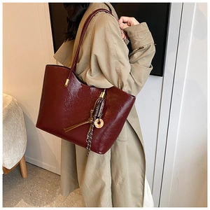 Détail d'un grand sac cabas bordeaux en cuir PU avec breloques sur trench beige