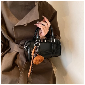Close-up of black patent leather boston bag with furry charm on a brown trench coat