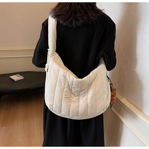 Rear view of model wearing a large cream quilted hobo bag with a cute bear charm