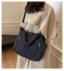 Detail of black quilted shoulder bag with diamond pattern on model in trench coat
