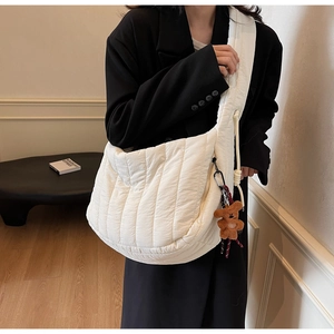 Close-up of white quilted crossbody bag with brown teddy bear charm and wide strap