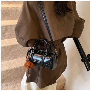Close-up of black cylinder bowling bag featuring a plush bear charm and crossbody strap