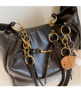 Detailed close-up of dark brown PU leather tote bag with gold metal chain and baseball charm