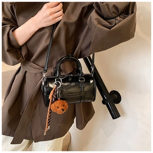Detail of black patent leather cylinder bag with bear charm worn with a brown trench coat