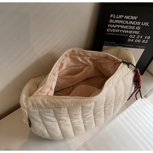 Detail of a beige quilted puffer bag featuring a spacious interior and zipper pocket