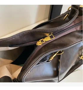 Detailed close-up of smooth brass metal zipper and stitching on dark brown PU leather bag