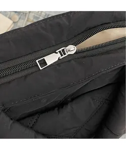 Detailed close-up of smooth silver metal zipper and black quilted fabric on shoulder bag