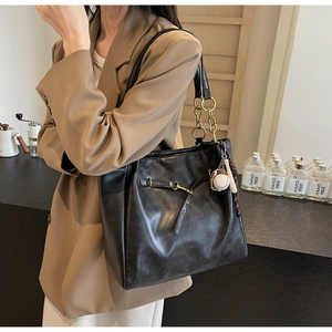Detail of black PU leather tote bag with metal chain strap and baseball charm accessory