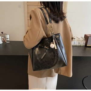 Detailed view of a large black PU tote bag with gold chain and baseball charm on a model