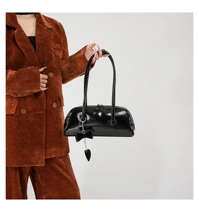 Detailed close-up of glossy black oil wax leather bag with ribbon bow and heart charm