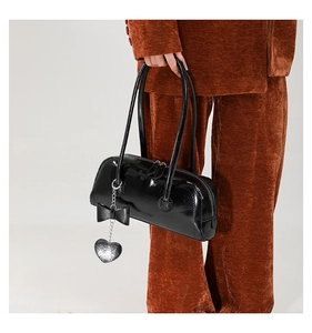 Close-up of black patent leather shoulder bag with bow and silver heart charm detail