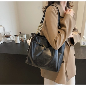 Detail of black faux leather tote with golden chain strap and baseball charm in cafe setting