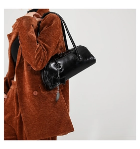 Detail of black glossy PU shoulder bag featuring bow pendant on caramel corduroy outfit