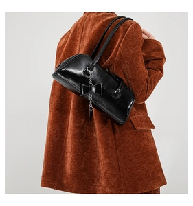 Detail of glossy black PU shoulder bag with bow charm and silver chain on model