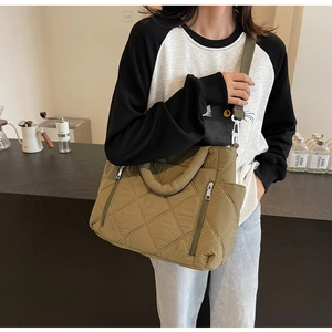 Olive green quilted tote bag with dual front zippers shown in a cafe setting