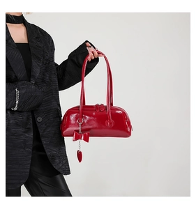 Detail of red patent leather handbag featuring bow and heart metal chain charms