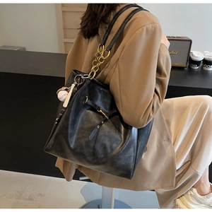 Detail of black PU leather tote with gold chain accent and baseball charm accessory