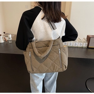 Detail of a brown quilted tote bag featuring classic diamond stitching and a metal zipper