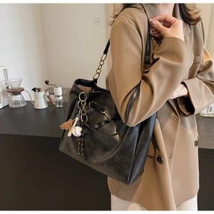 Detail of black PU leather tote bag with unique baseball charms and chain strap