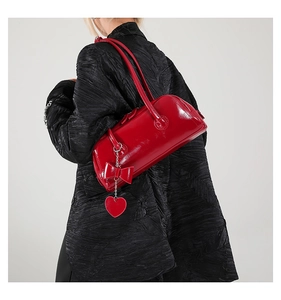 Detail of red glossy PU shoulder bag featuring a decorative bow and heart-shaped pendant