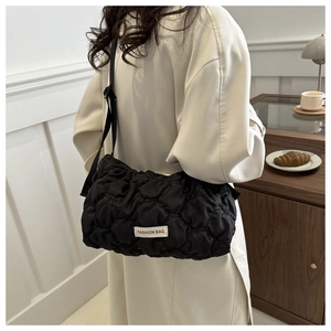 Detail of black quilted shoulder bag featuring fashion label and adjustable strap