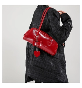 Detail of red patent leather shoulder bag featuring a large bow and heart charm on a model
