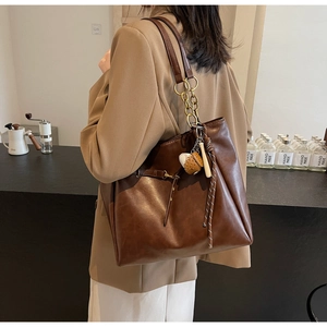Detail of deep brown PU leather tote bag with gold chain and baseball charm