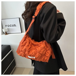 Detail of orange quilted shoulder bag with white FASHION BAG label and adjustable strap