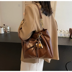 Detail of a dark brown vintage PU leather tote bag with a baseball charm and tassels