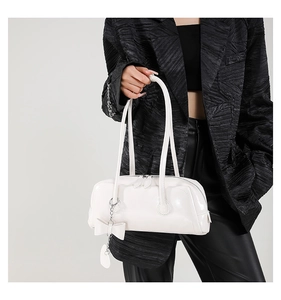 Detail view of a white patent leather shoulder bag with bow charm and silver chain