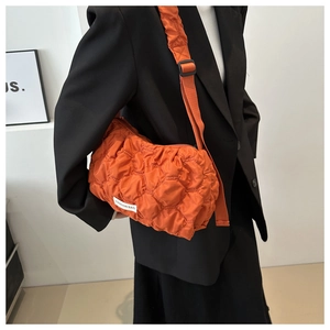 Detail of orange quilted puffer bag with white fashion tag and adjustable shoulder strap