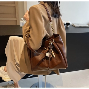 Detail of brown matte PU leather tote bag with gold chain strap and baseball pendant