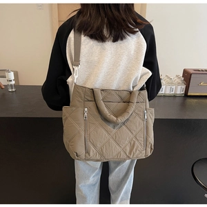 Detail of coffee brown quilted tote bag with side zippers and adjustable strap on a model
