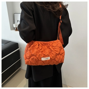 Detail view of orange quilted puffer bag with crossbody strap and fashion woven label